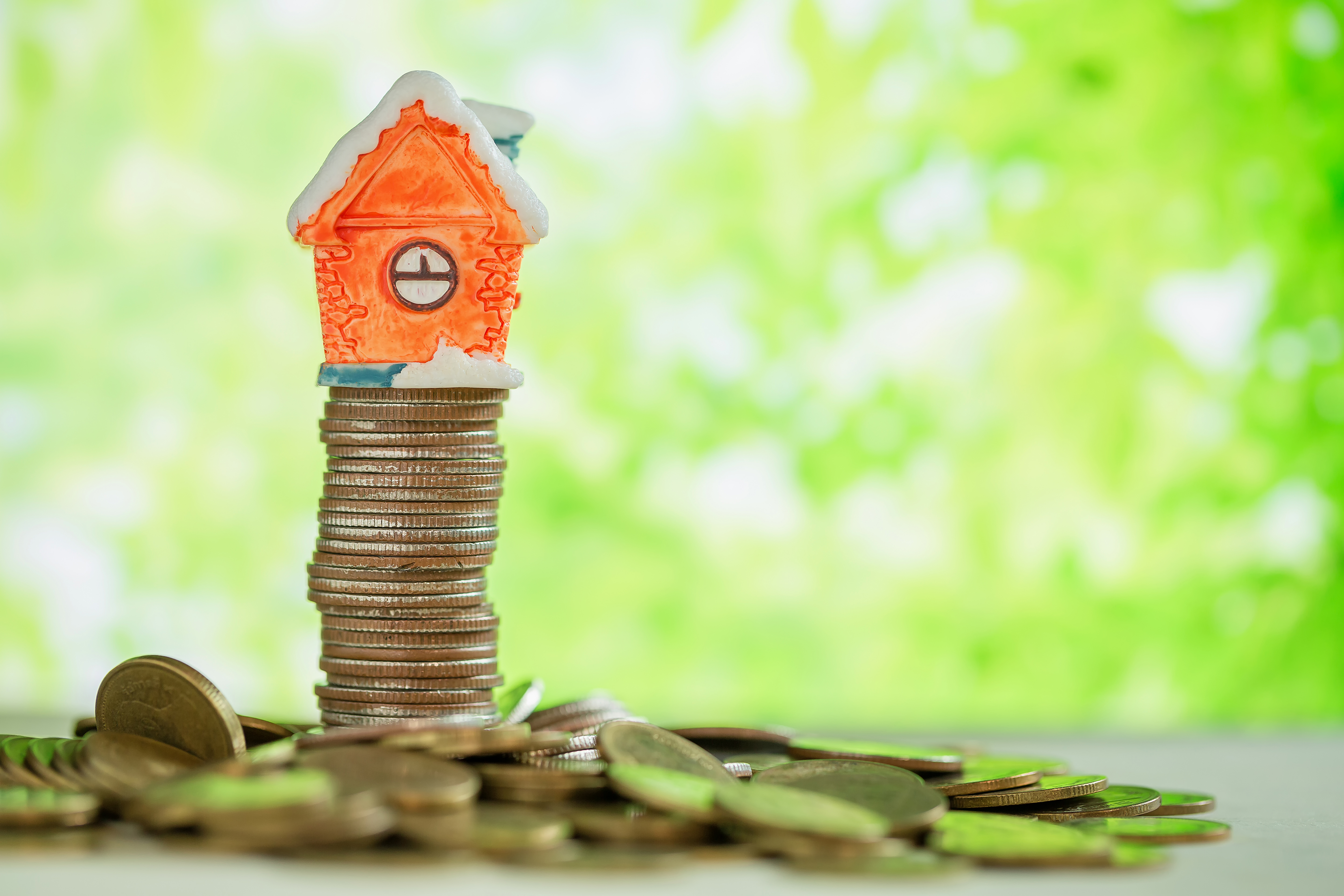 Mini house on stack of coins with green blur background.