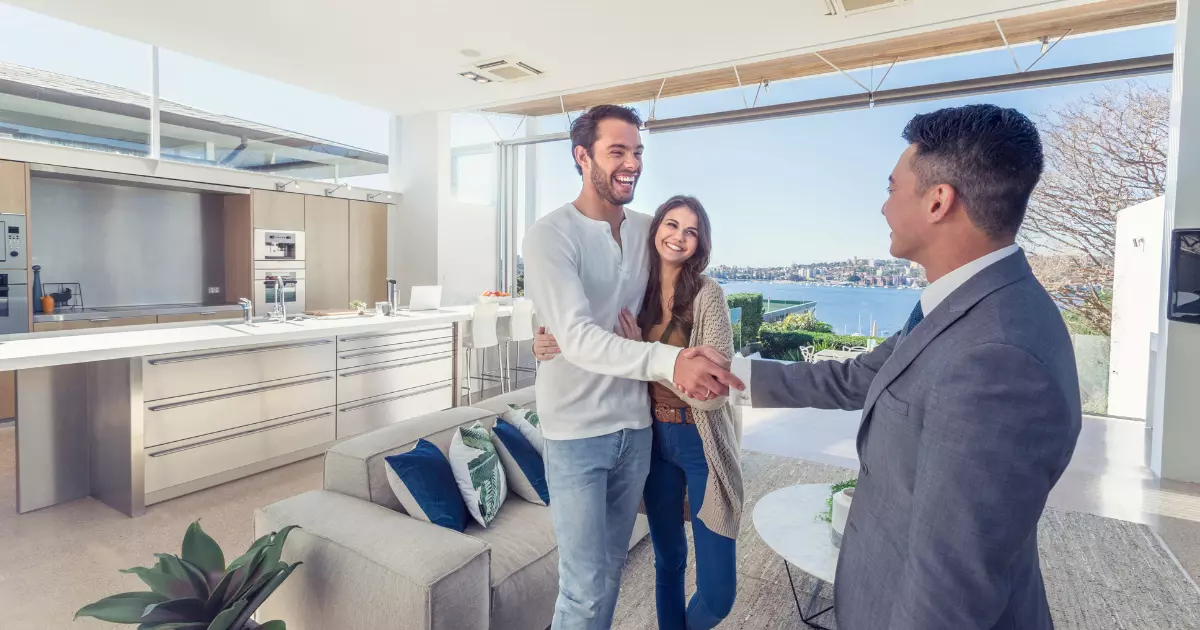 A real estate agent shaking hands with a couple of people in a room with a lake